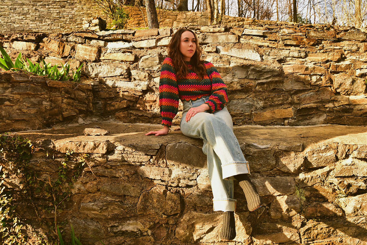 Singer Sarah Jarosz sitting on a rock wall.
